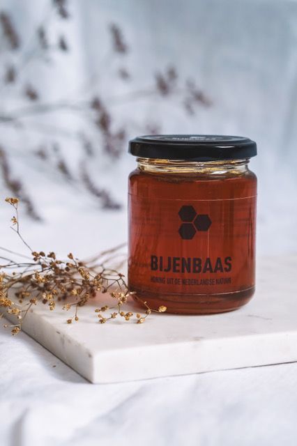 Glazen pot met amberkleurige honing en een zwart deksel op een witte marmeren plaat, tegen een zacht vervaagde achtergrond.