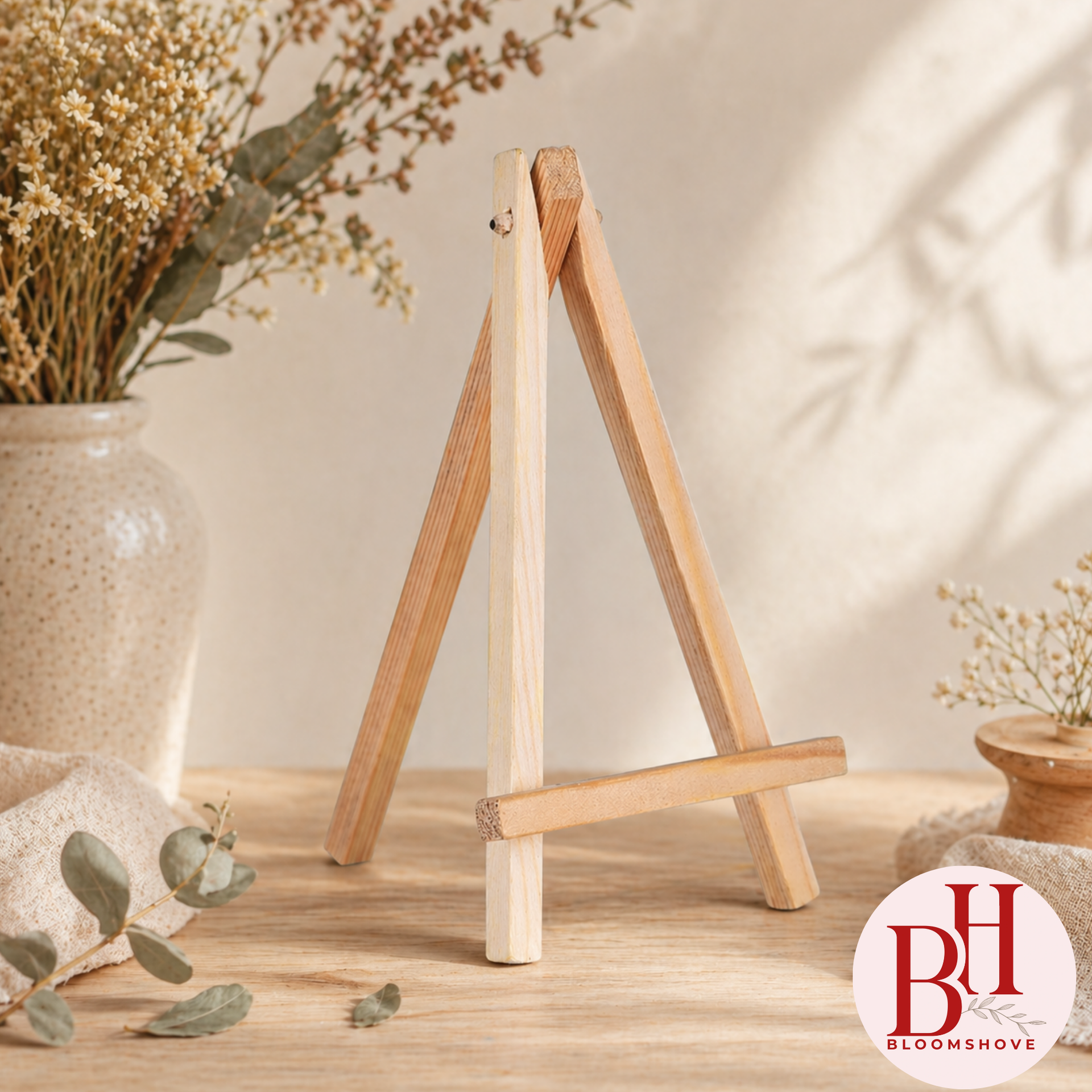 Houten schildersezel op een licht bureau met gedroogde bloemen en zachte beige decoratie.