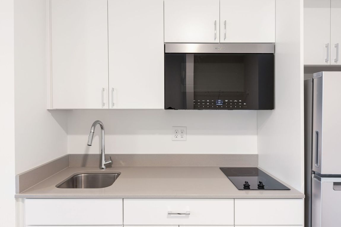 Small, modern white kitchen with microwave, sink, and cooktop.