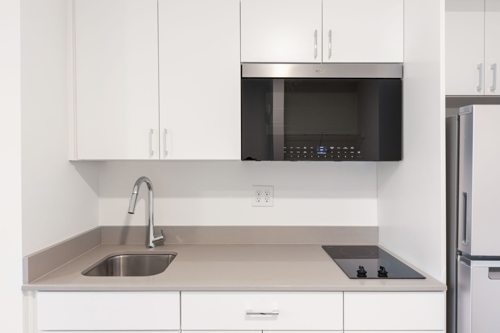 Small, modern white kitchen with microwave, sink, and cooktop.