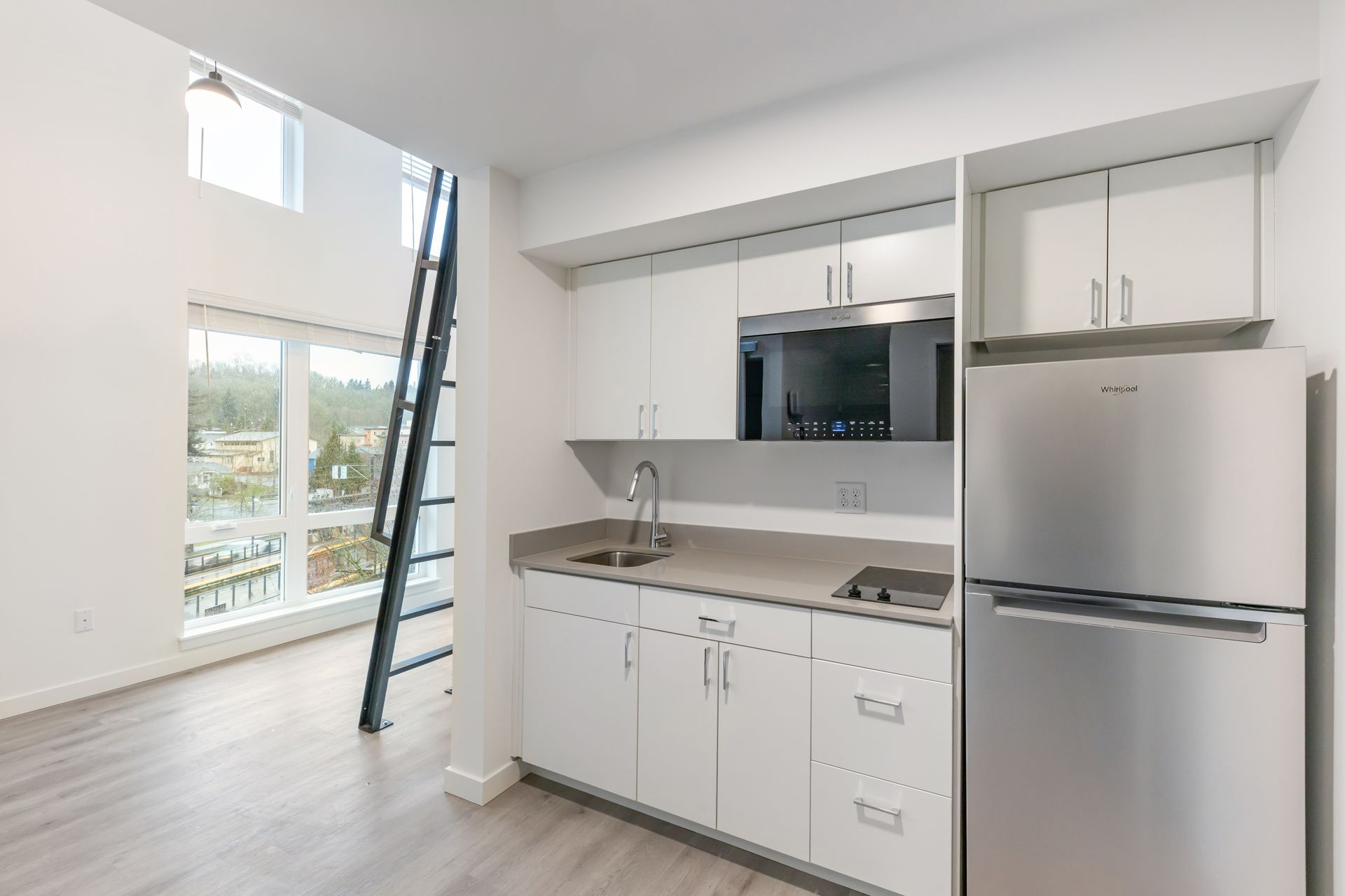 Small white kitchen with stainless steel fridge, stove, and ladder to upper level.