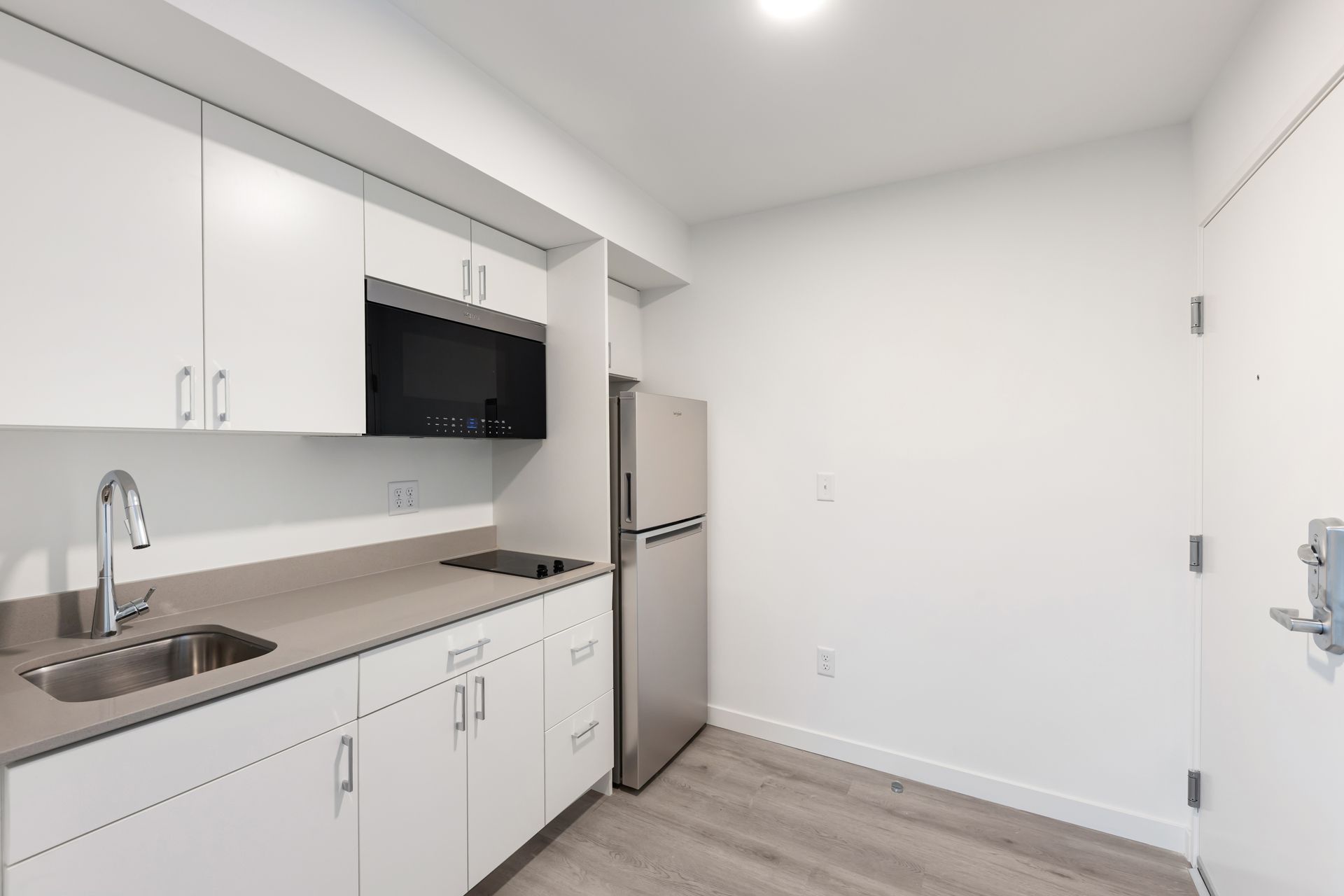 Small white kitchen with countertop, cabinets, microwave, refrigerator, and silver faucet.