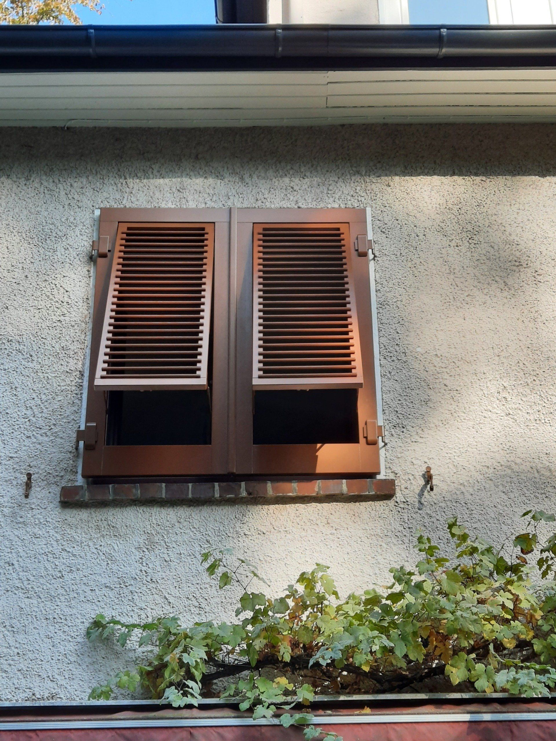 Ein Fenster mit braunen Fensterläden an einer grauen Wand
