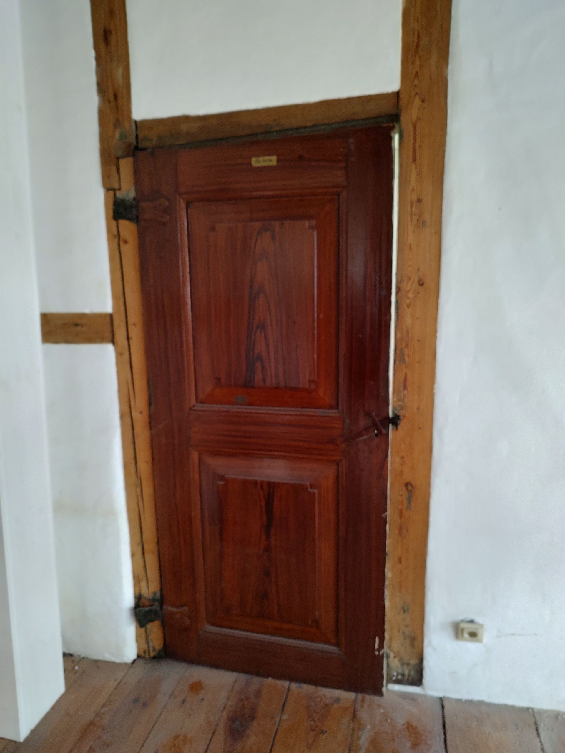 In einem Raum mit Holzboden steht eine Holztür offen.