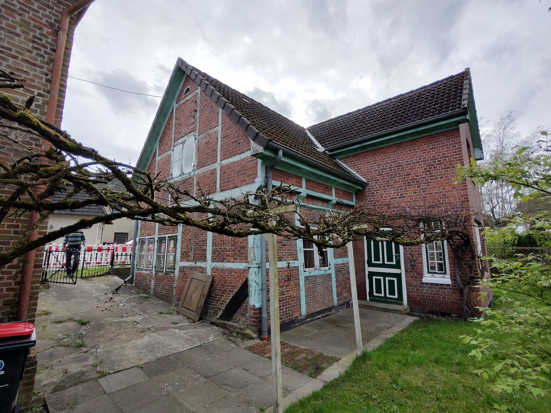 Ein Backsteinhaus mit grünem Dach und einem Baum davor.