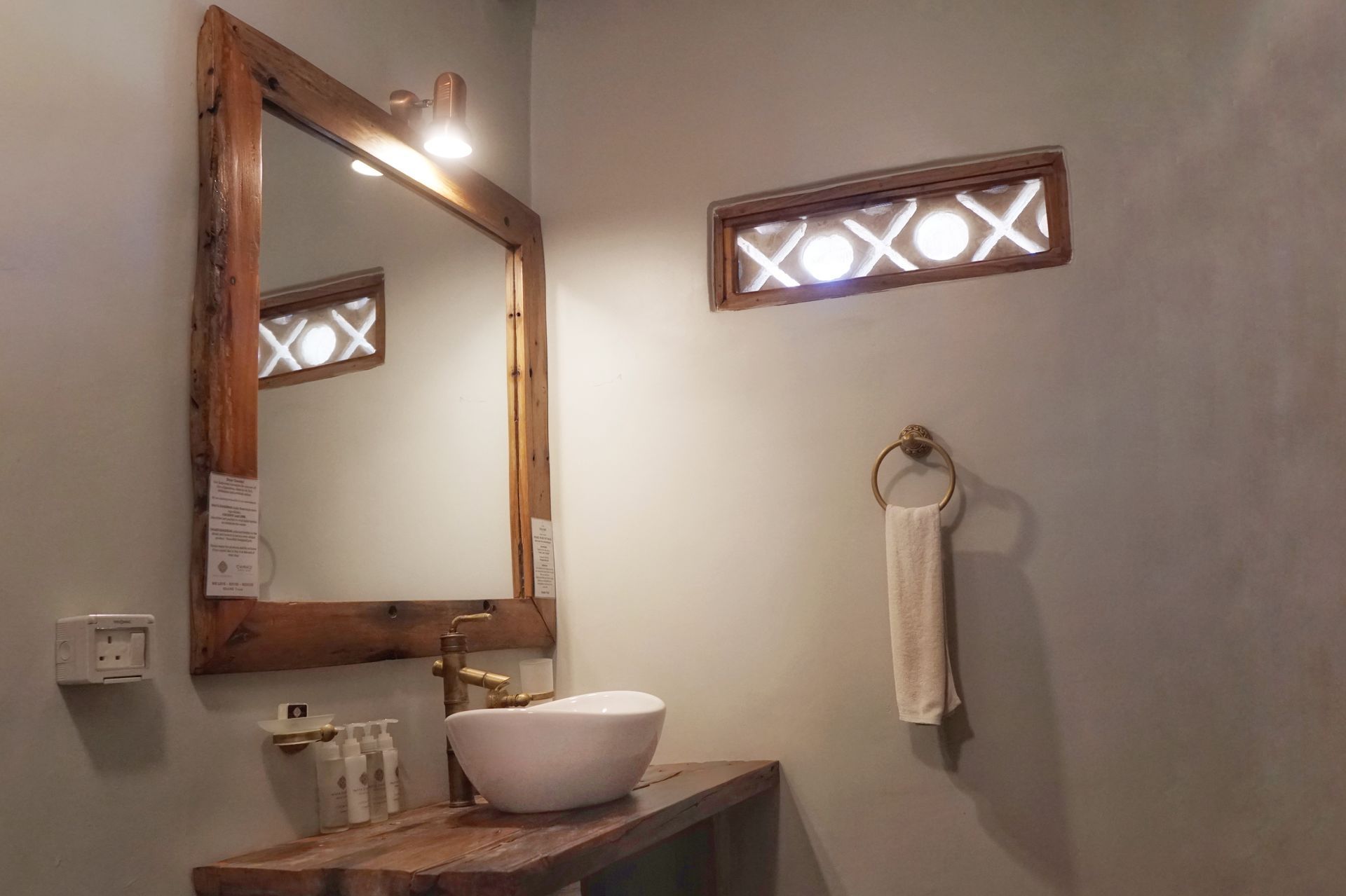 Small rustic bathroom with wooden mirror, vessel sink, wall light, and towel ring.