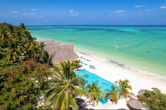 Tropical beach resort with turquoise water, white sand, palm trees, and a pool overlooking the sea