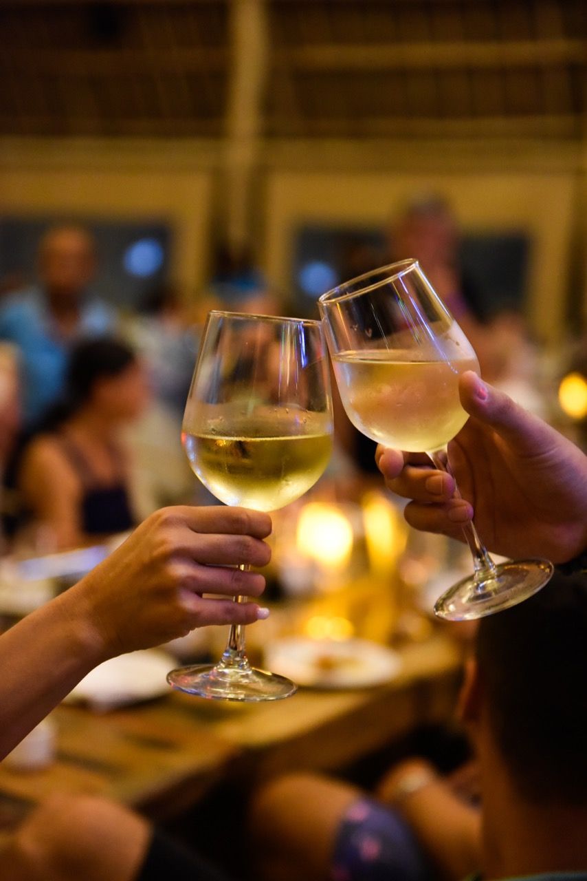 Two hands toasting with white wine glasses in a softly lit restaurant