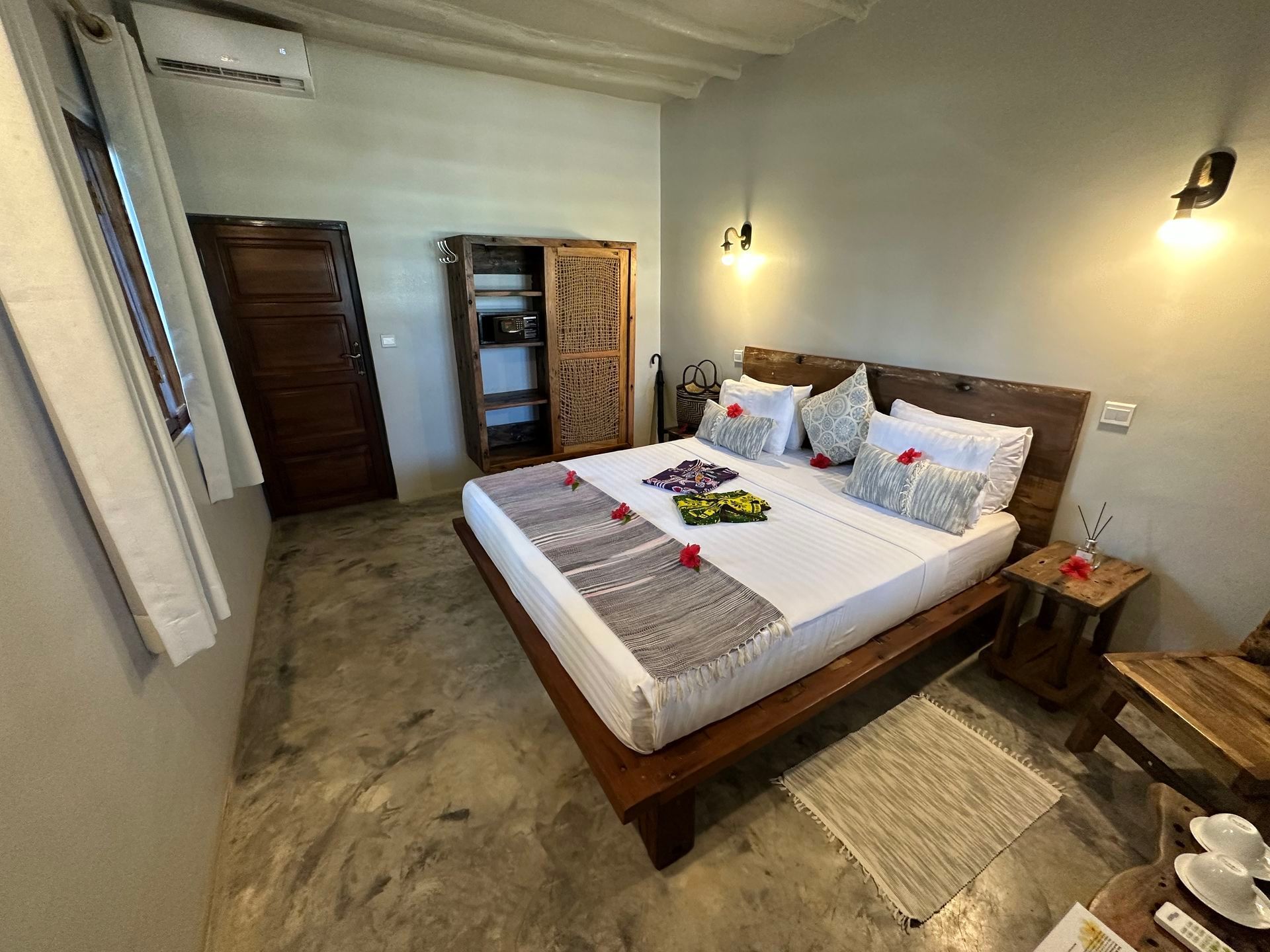 Bedroom with wooden bed, white linens, wall lamps, wardrobe, and stone floor in a rustic room