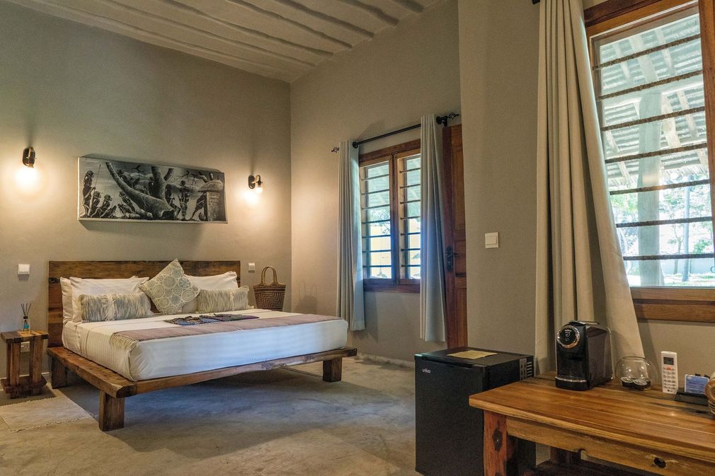 Warm bedroom with a wooden bed, beige walls, windows, curtains, and a desk in the foreground