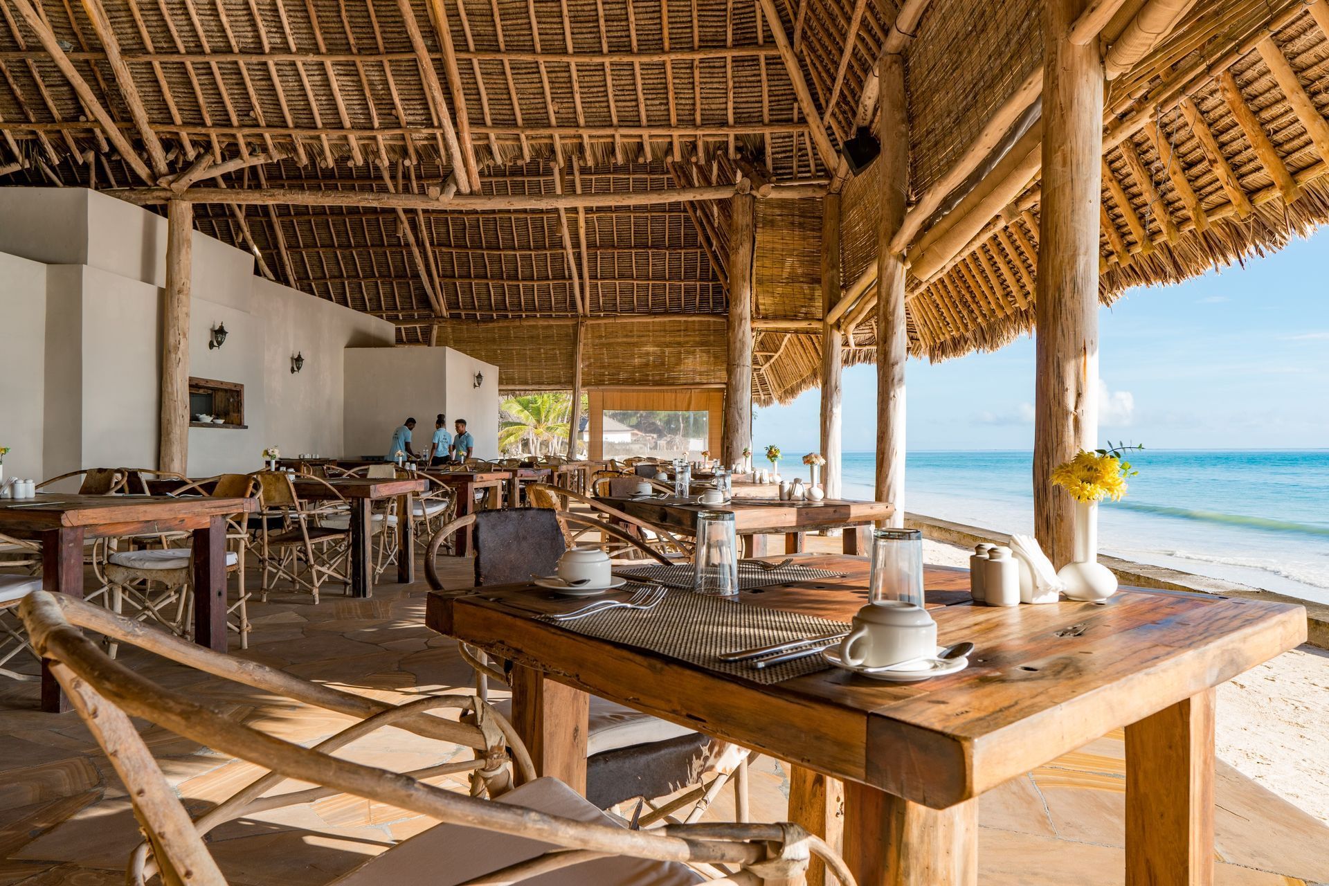Open-air beachside restaurant with wooden tables and chairs overlooking the ocean