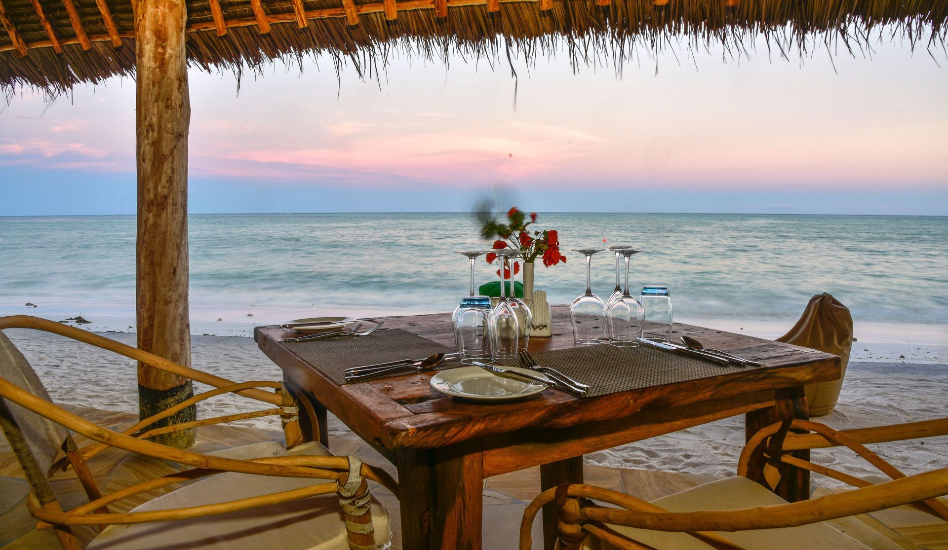 Beachfront dining table with flowers and candles, facing the ocean at sunset