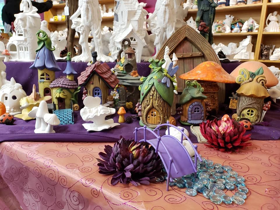 Ceramic fairy houses and mushrooms on a table with flowers and a bridge, in a shop.