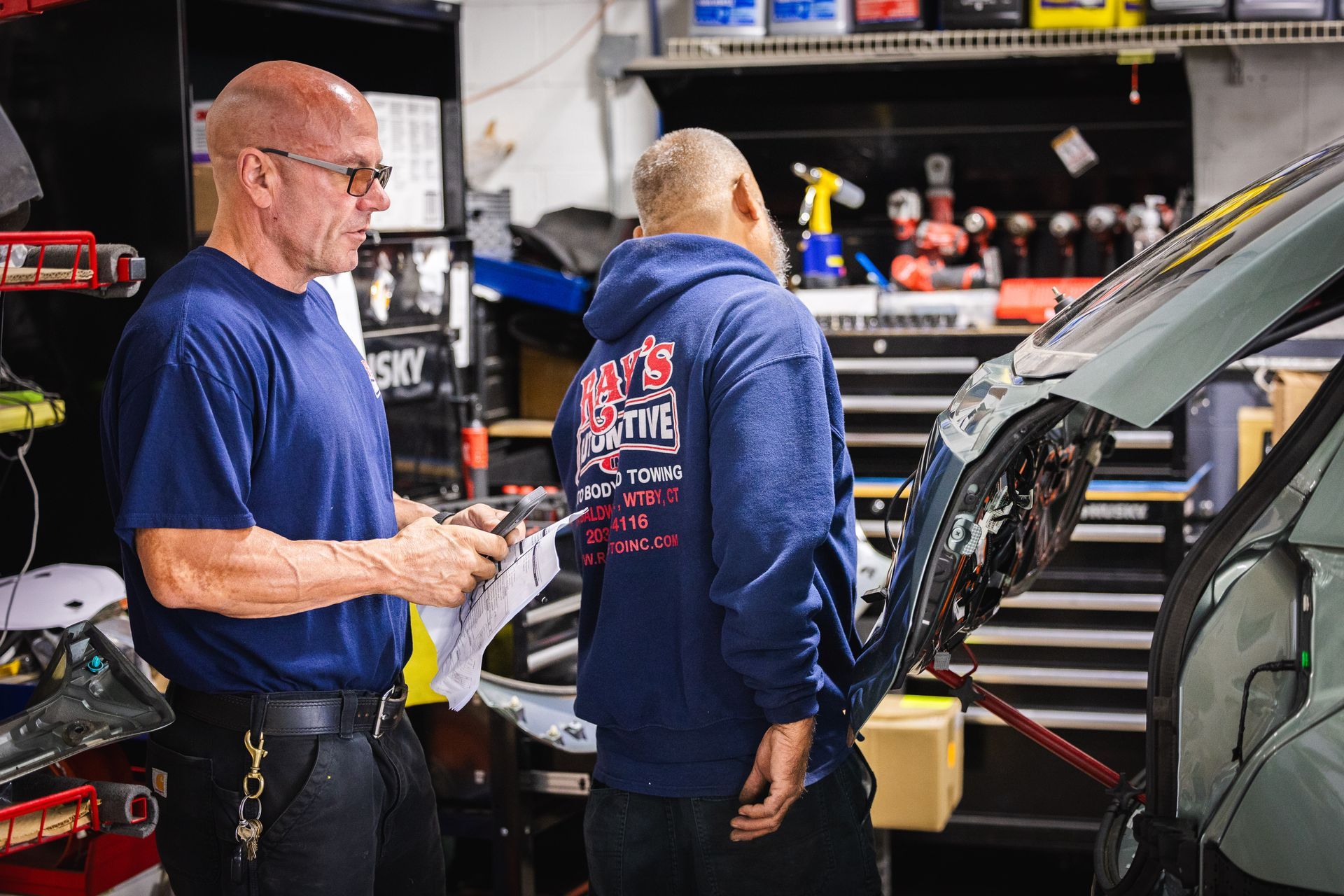 Worker in red safety vest inspecting a silver car body in an auto repair shop