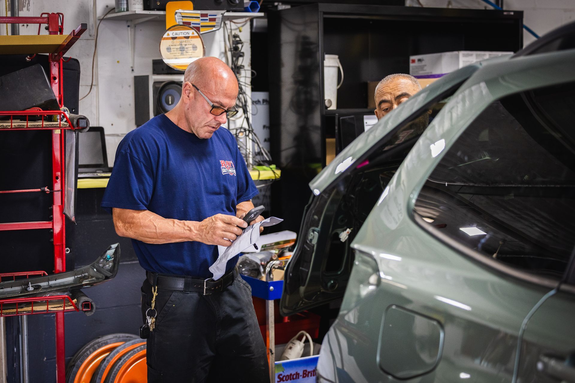 Mechanic in a blue shirt working beside a green car in a garage