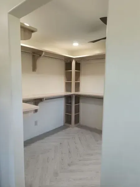 Empty walk-in closet with white shelves, hanging rods, and light gray herringbone flooring.