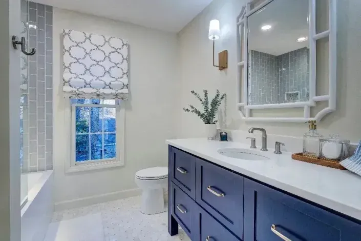 Bright bathroom with navy vanity, white countertop, mirror, window shade, and bathtub shower on the left