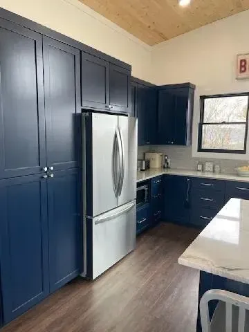 Modern kitchen with dark blue cabinets, stainless steel fridge, wood floor, and light countertops.