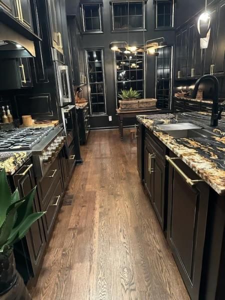 Narrow galley kitchen with dark cabinets, marble countertops, wood floor, and a windowed back wall.