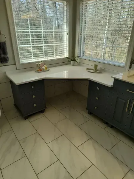 Corner bathroom vanity with gray cabinets, white countertop, and large windows over tiled floor