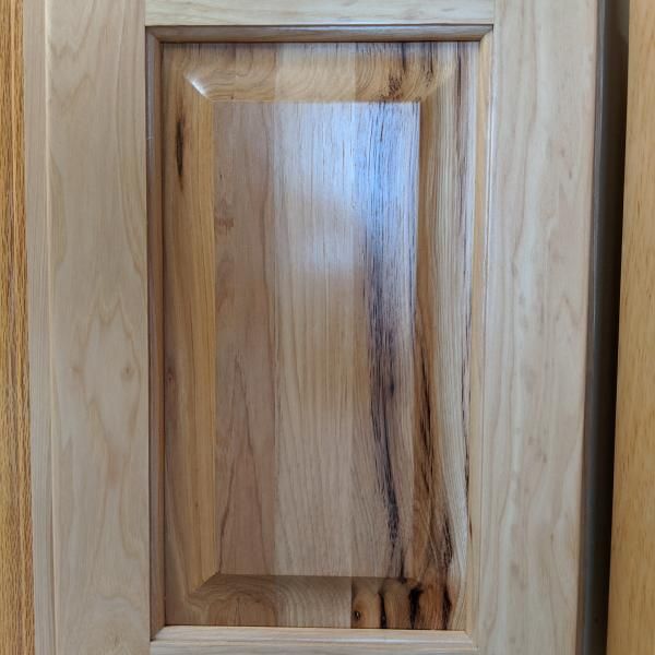 Close-up of a light wood cabinet door with a raised panel and dark wood grain streaks.