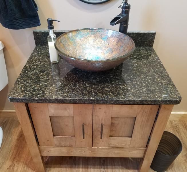 Bathroom vanity with granite countertop and round vessel sink, featuring wooden cabinet doors and a soap dispenser