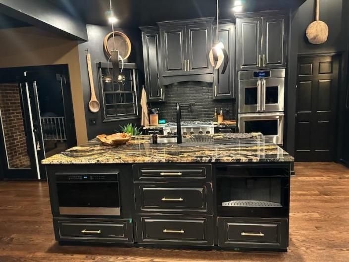 Modern kitchen with dark cabinets, granite island, stainless appliances, and warm pendant lighting