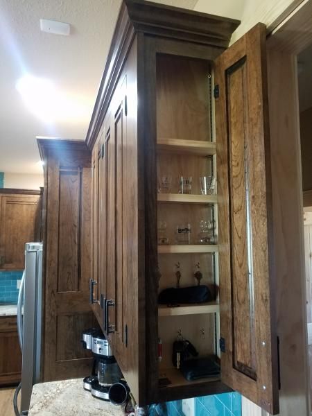 Wooden kitchen cabinets with a pantry door open, showing shelves, dishes, and bottles.