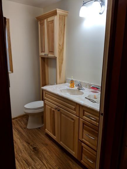 Small bathroom with wood vanity, white countertop, and toilet beside a tall cabinet.