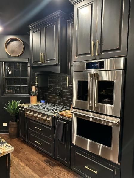 Modern dark kitchen with black cabinets, stainless steel double oven, gas range, and tiled backsplash
