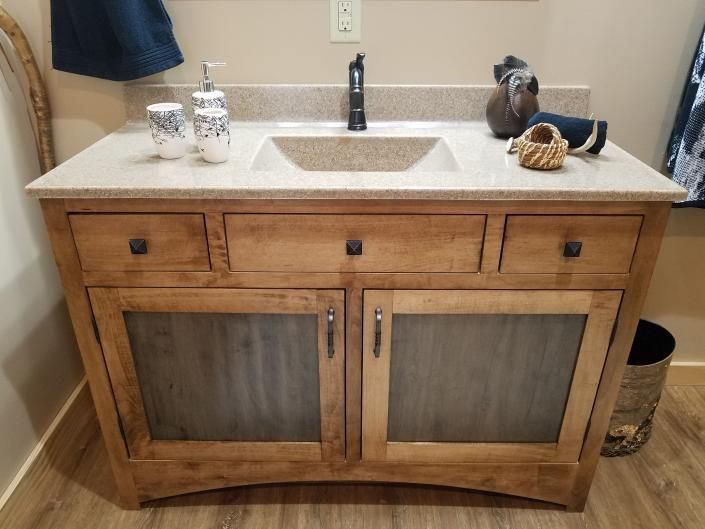 Wood bathroom vanity with beige countertop, white sink, black faucet, and decorative items on top