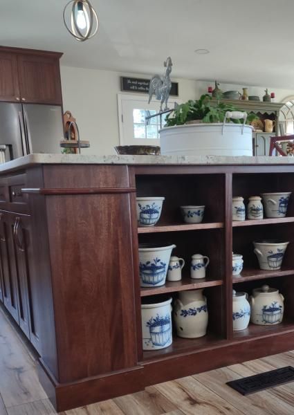 Kitchen island with open shelves displaying ceramic bowls and mugs, with a planter and stainless refrigerator nearby