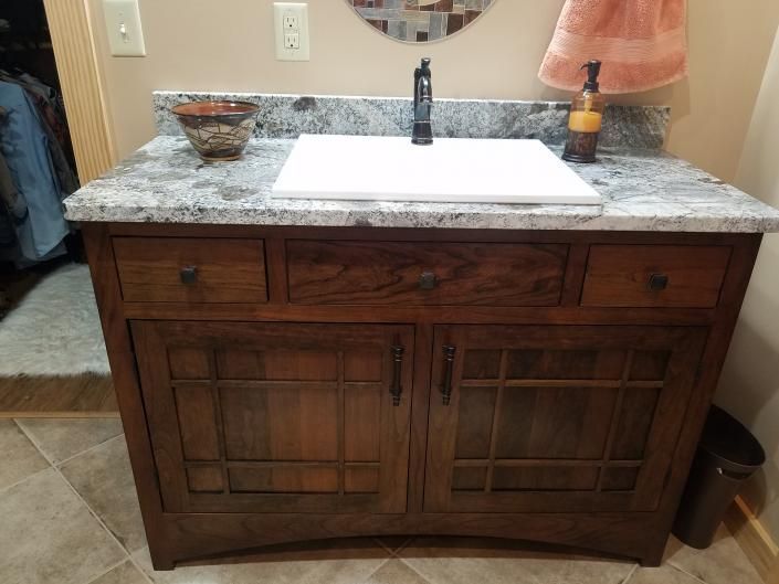 Wooden bathroom vanity with granite countertop, white sink, and bronze faucet beneath a round mirror