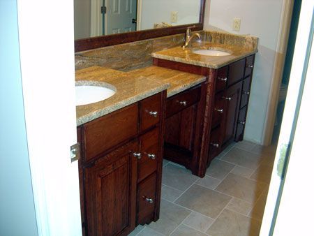 Bathroom vanity with two sinks, granite countertop, and dark wood cabinets in a tiled room