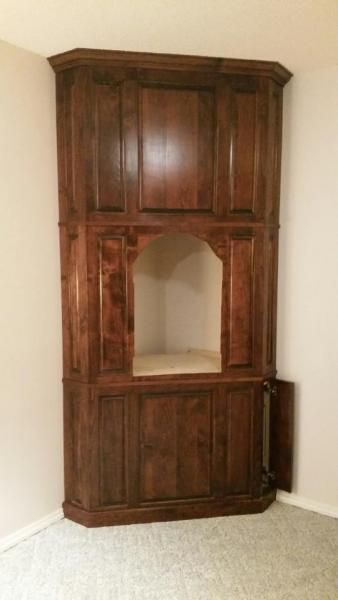 Dark wooden corner cabinet with an open center shelf against a beige wall and carpet.