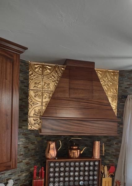 Decorative copper range hood above a stove with stone backsplash and patterned gold wall panels