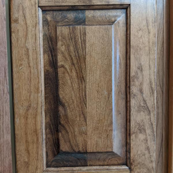 Close-up of a wood cabinet door with a raised rectangular panel and dark grain accents