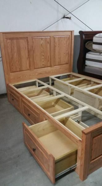 Wooden bed frame with open drawers and storage compartments in a room.