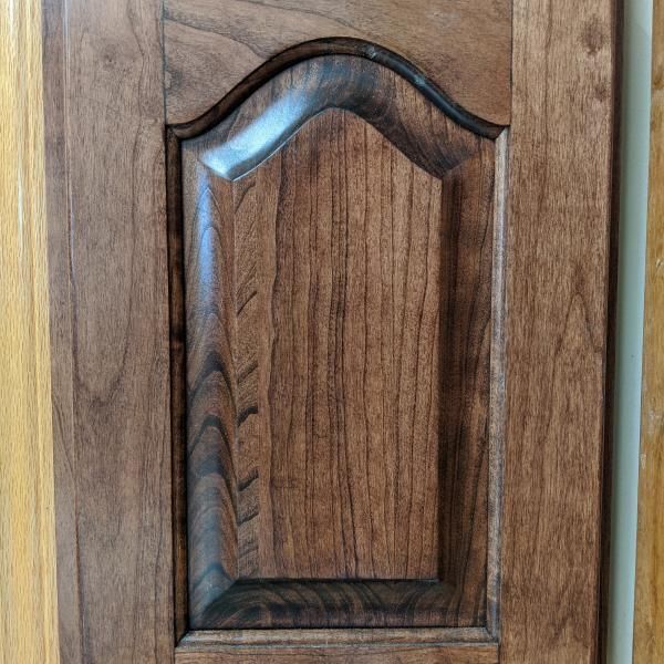 Wooden cabinet door with carved arched panel and dark wood grain.