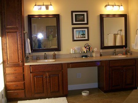 Double bathroom vanity with two mirrors, wall sconces, and wooden cabinets in a warmly lit room