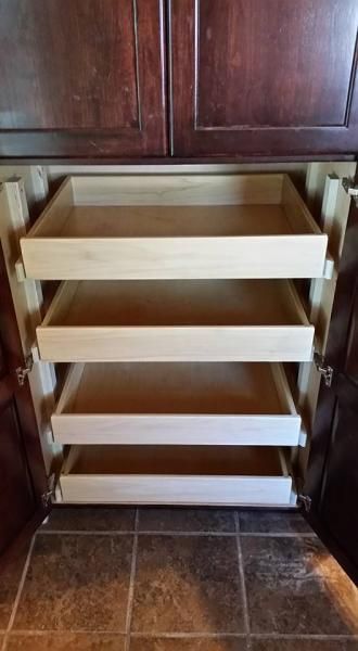 White pull-out pantry drawers inside a dark wood cabinet on a tiled floor.