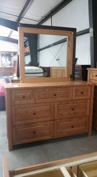 Wooden dresser with mirror in a furniture showroom, with other furniture nearby.