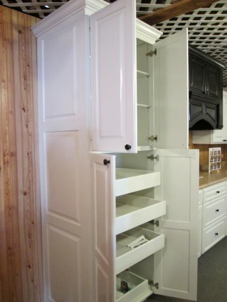 Tall white kitchen pantry cabinet with pull-out shelves beside wood paneling