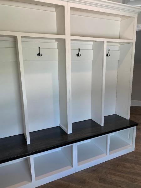 White mudroom cubbies with black bench and hooks, featuring storage cubbies above and below.
