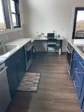Narrow modern kitchen with blue cabinets, white counters, and a small desk at the far end