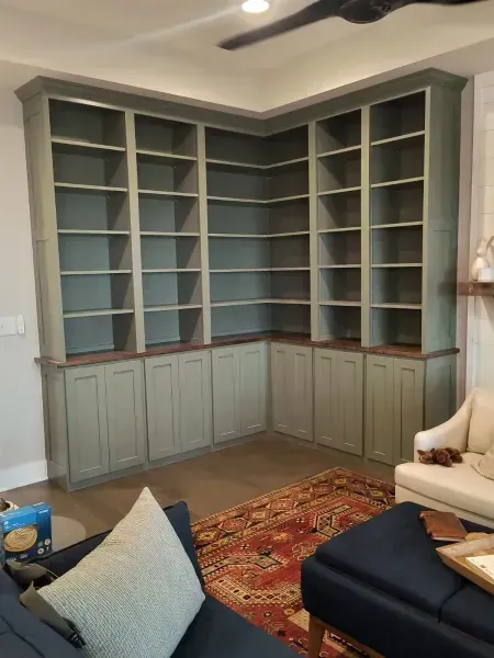 Built-in sage green corner shelving and cabinets in a living room, with rug and sofa visible