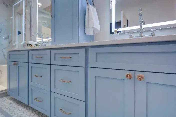 Light blue bathroom vanity with drawers, cabinet doors, and a white countertop beside a glass shower door
