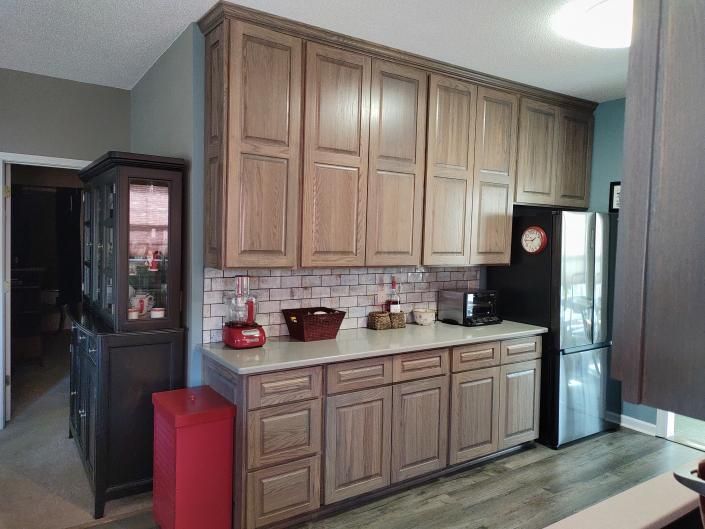 Kitchen with wood cabinets, black refrigerator, and red trash bin next to a sink and countertop.