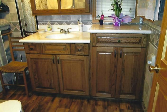 Wooden bathroom vanity with sink, mirror, cabinets, and purple flowers on the windowsill.