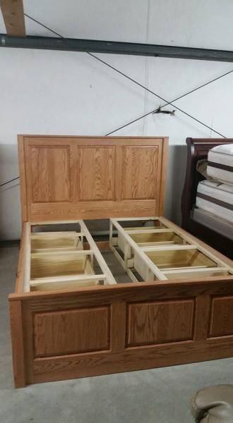 Wooden bed frame with open storage compartments in a workshop or showroom.